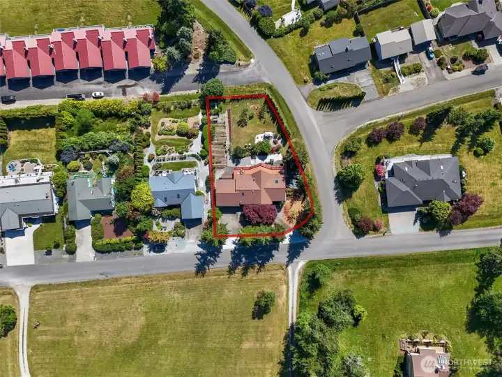 Aerial view showcasing the beautifully landscaped corner lot, raised garden beds, greenhouse, and established gardens.