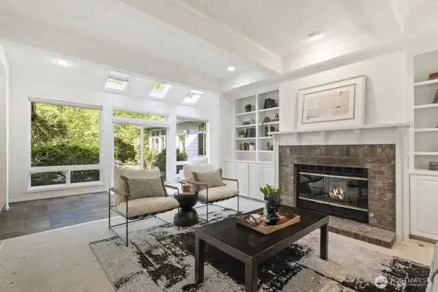 Large informal gathering room with a beam ceiling with crown molding, gas brick surround fireplace flanked by white built-ins.
