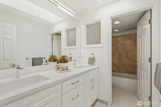An updated hall bath with new quartz vanity, tile floor, new lighting and solid surface surround tub/shower.