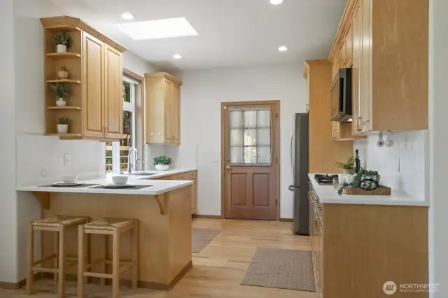 Kitchenette with bar seating, quartz counters, maple cabinetry and east facing door the front exterior.