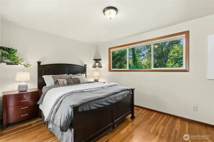 Spacious primary bedroom with large picture window and hardwood floors. Spacious primary bedroom with large picture window and hardwood floors.