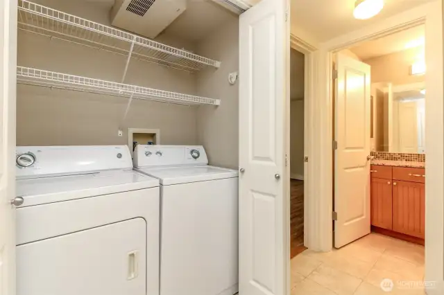 Full-size washer-dryer with storage shelves hides behind closet doors.
