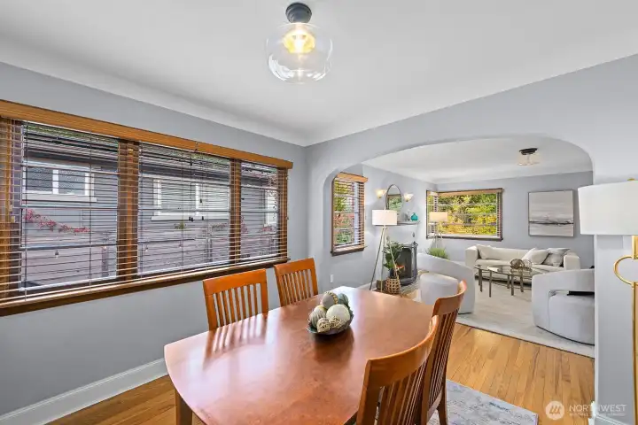 Bright dining area with rich hardwood floors and classic arched entryway opening to cozy living room. Large windows bring in abundant natural light