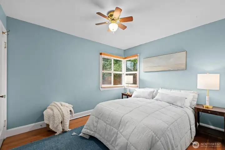 Secondary bedroom with hardwood floors, calming blue walls, and corner windows that bring in abundant natural light