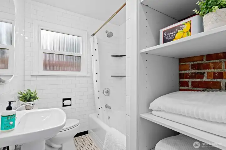 Bright full bath with classic white subway tile, vintage details, and built-in shelving accented by exposed brick for timeless charm