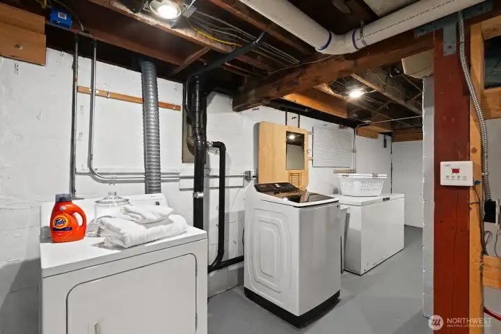 Convenient lower-level laundry area with washer, dryer, utility sink, and ample space for folding and storage—clean, functional, and move-in ready
