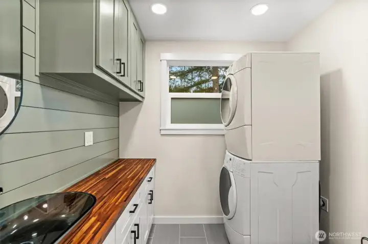 Dedicated laundry with stacked washer/dryer, butcher block folding counter, and cabinetry