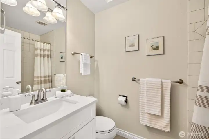 The full hall bath is bright and clean, featuring a wide vanity with generous counter space, modern lighting, and crisp fixtures. A tub and shower combo with tile surround makes this bathroom practical for everyday use, guests, and weekend routines.