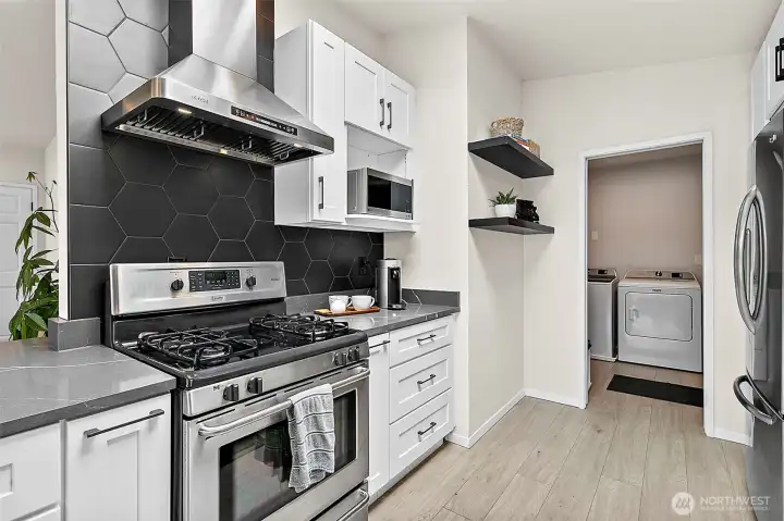 Gas range, stainless hood, tile backsplash, and nearby laundry access.