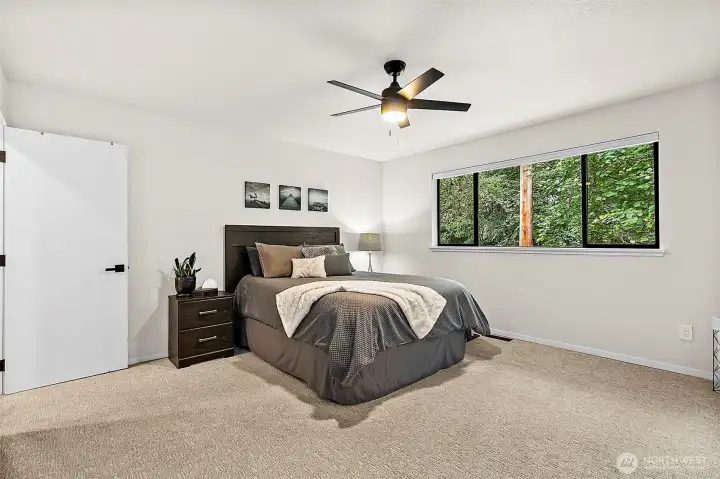 Comfortable bedroom with ceiling fan and peaceful green outlook.