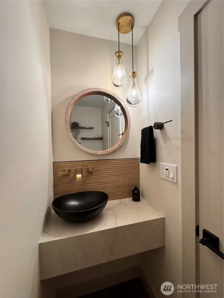 Luxe powder room with floating stone vanity, black vessel sink, wood slat accent wall, designer mirror, and statement lighting.