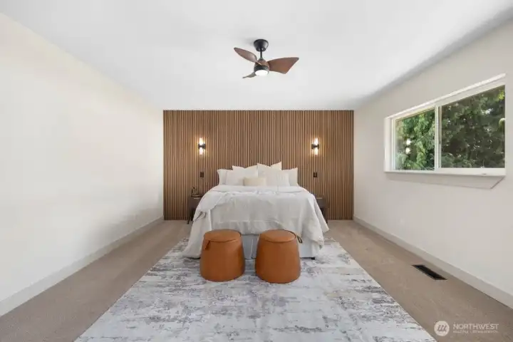 Oversized primary suite with custom wood feature wall, integrated accent lighting, designer sconces, and warm modern finishes.