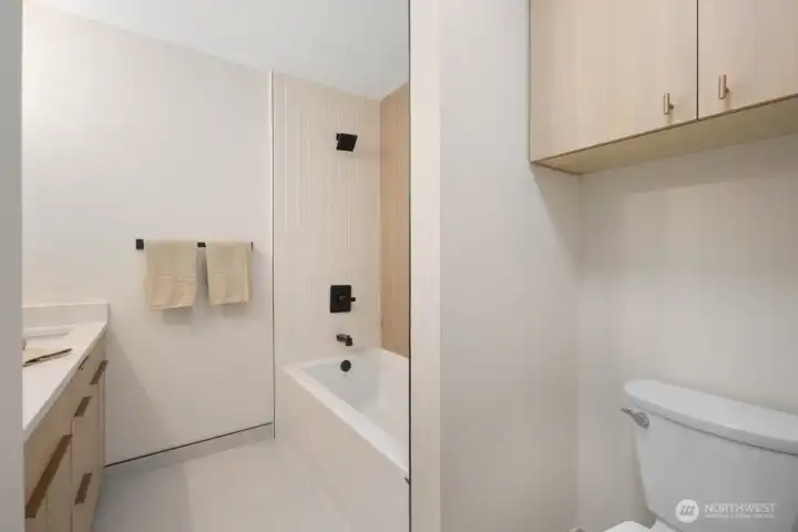 Luxurious primary bath featuring deep soaking tub, custom tile work, wood-look accent wall, matte black fixtures, and dual vanity and outlet for bide