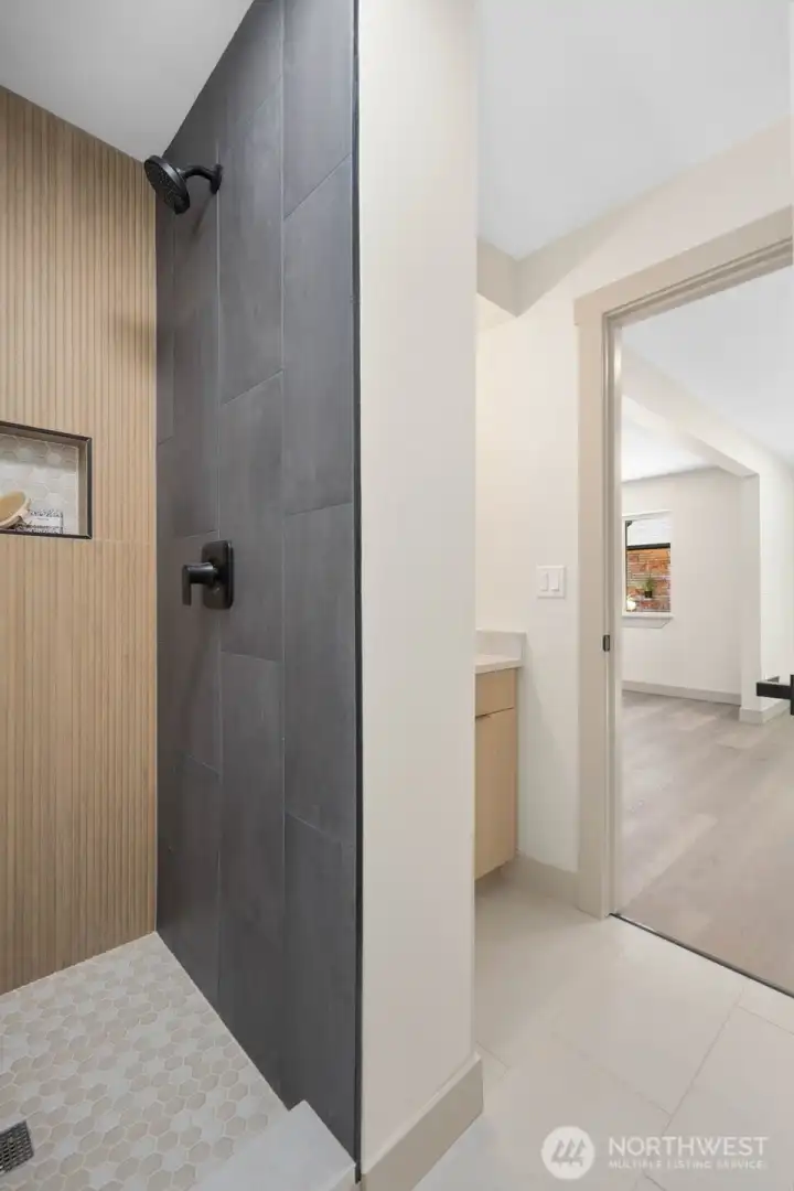 Custom tiled shower with wood-look accent tile, dark feature wall, hex tile floor, niche, and matte black fixtures