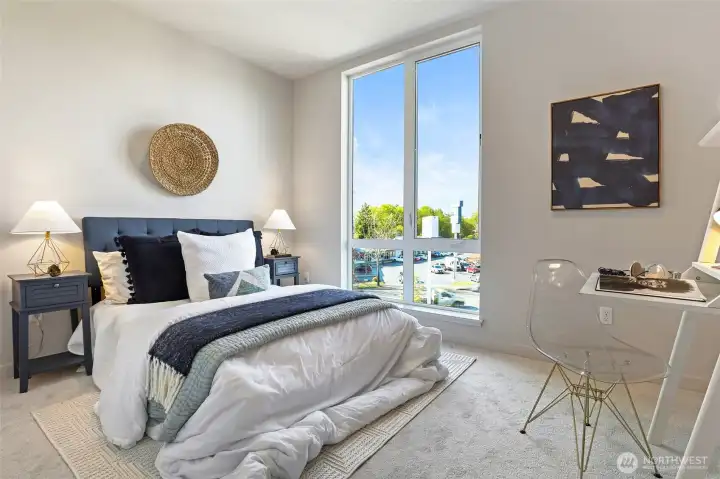 A sunlit bedroom designed for comfort, with oversized windows, plush carpeting, and space for a desk, is the perfect work-from-home or guest retreat.