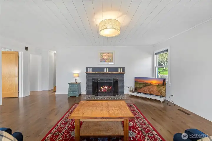 Spacious, light filled living room with painted wood plank ceilings and a real wood fireplace.