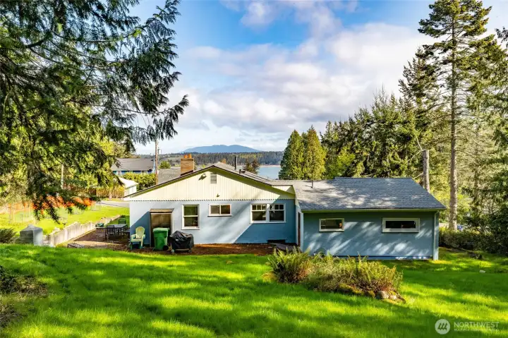 Back of the home. Photo taken from the back lot that is also included in the sale. Level cement patios and fire pit. Water view in the distance.