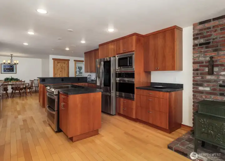 Kitchen area showing eating bar as well as pantry (far wall). Double oven on the island, plus 3rd oven & microwave on the cabinet wall. Extensive Maple hardwood flooring throughout