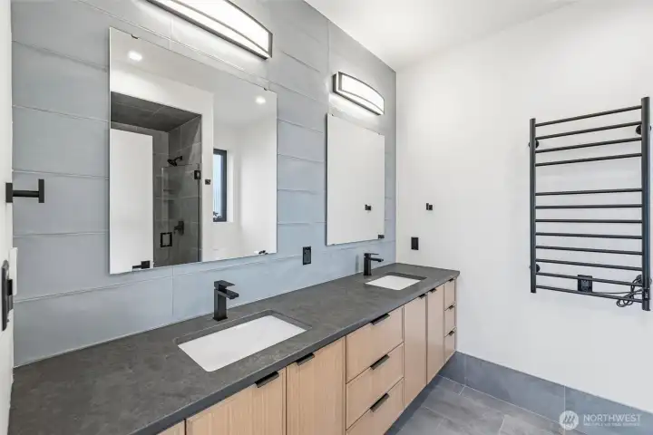 Primary bath with dual sinks, quartz countertops, full tiled wall and heated towel bar.