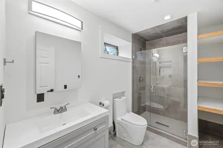 Bathroom off the recreation room with tile shower, storage shelves and heated tile floors.