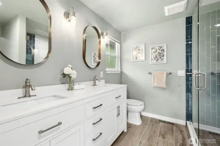 Beautifully remodeled primary ensuite blending clean contemporary design with warm, timeless finishes. Features include a sleek dual-sink vanity with quartz counters, modern framed mirrors, stylish lighting, abundant storage, and luxury plank-style tile flooring. The oversized walk-in shower is finished with elegant tile surrounds and glass enclosure, creating a spa-inspired retreat filled with natural light and sophisticated detail.