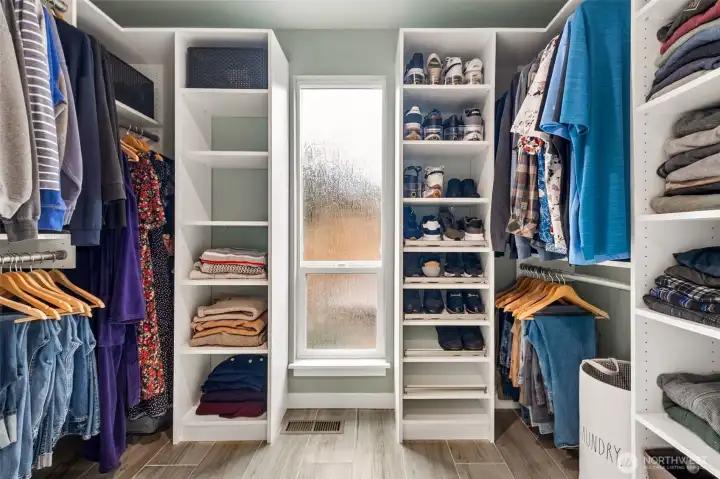 Customized walk-in closet thoughtfully designed with extensive built-ins, open shelving, multiple hanging areas, and dedicated shoe storage for exceptional organization. A frosted daylight window fills the space with soft natural light, while the clean contemporary finishes create a bright, boutique-style dressing area with both beauty and functionality.