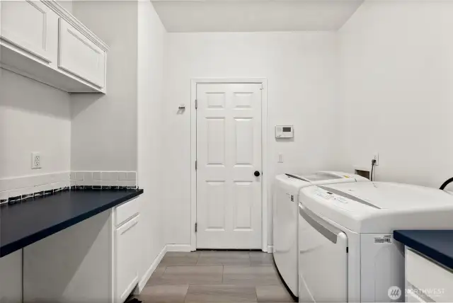 Clean and functional laundry room comes with loads of storage and convenient folding counter.