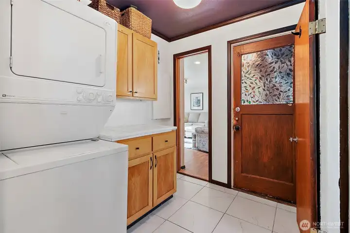 Utility room with stacked laundry machine in between main house and extension/rec room in back. Tile floor with storage cabinets and working countertop space.