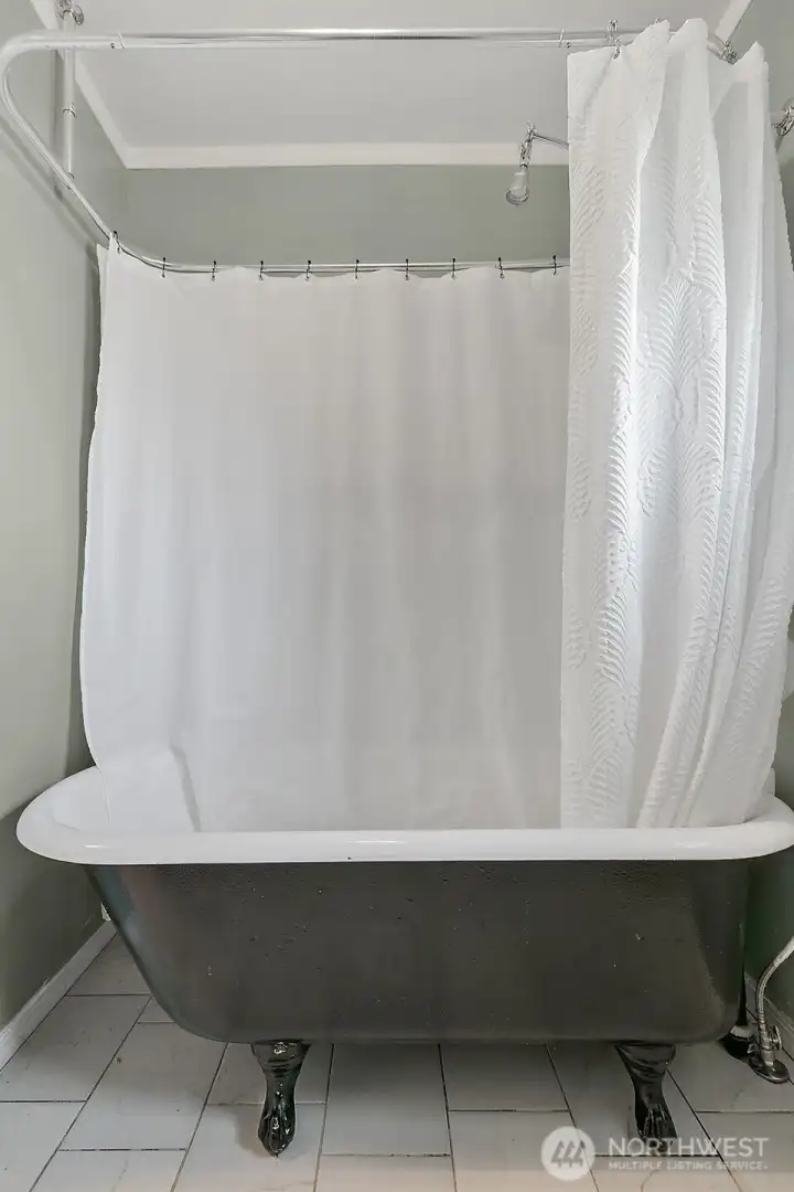 Clawfoot tub with wrap around shower curtain rod and over hanging showerhead. Tile floors.