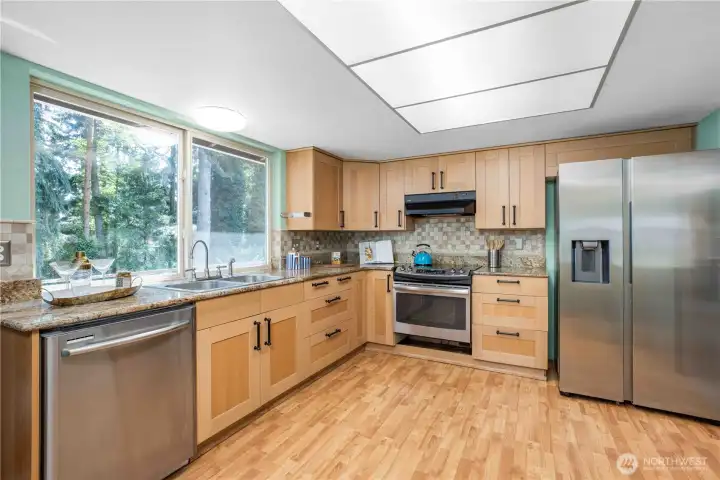 Kitchen view from the Dining Room. Large window over the sink that overlooks the spacious deck backyard. Kitchen is equipped with a side-by-side stainless steel refrigerator, stainless steel dishwasher, and stainless steel stove.