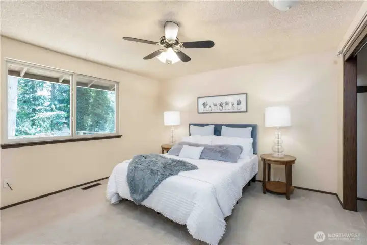 Primary bedroom with a ceiling fan and large window that overlooks the backyard.