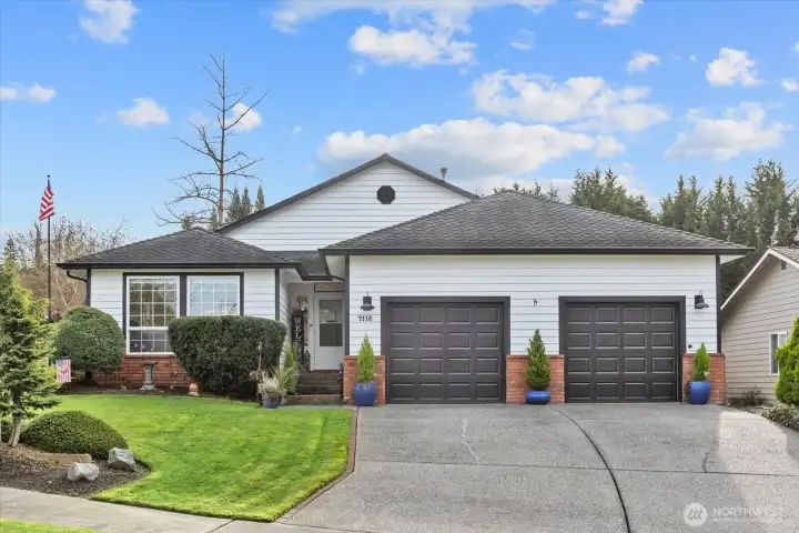 A beautifully maintained front exterior featuring crisp white siding, black accents, and a welcoming covered entry. The manicured lawn, mature landscaping, and charming front-porch décor create inviting curb appeal.