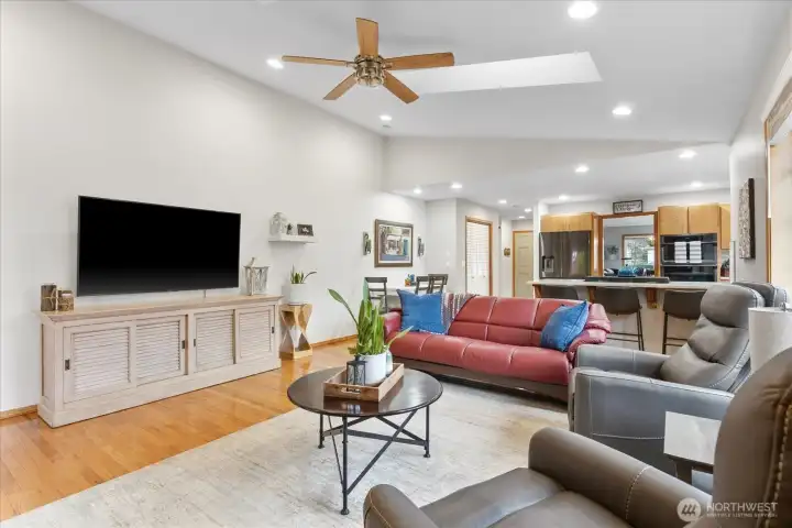 Bright and functional open layout showcasing the living room, dining nook, and kitchen. The space features hardwood floors, a large picture window, stainless steel appliances, and a central island with bar seating. Perfect for everyday living and hosting gatherings.