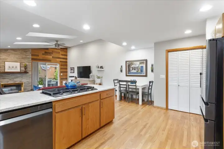 Central island with gas cooktop and quartzite countertop. Adjacent dining area includes space for a table and direct sightlines into the living room.