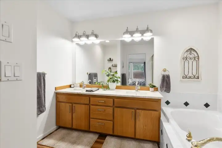 Bathroom featuring a double-sink vanity with ample storage, large wall mirror, and overhead lighting. Tile surround extends to the adjacent jetted tub.