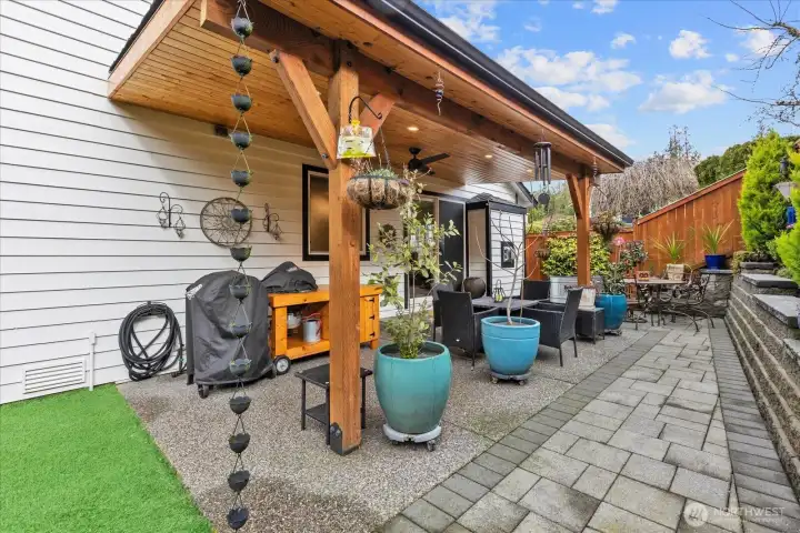 Outdoor living space featuring covered grilling area, seating zones, and decorative planters. Textured concrete and stonework define the layout.