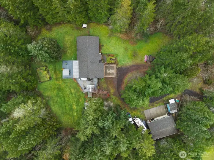 Aerial view showcasing garden space, partially covered huge deck, dog kennels, shop, three outbuildings, two RV spots, and private walking trail along the property.