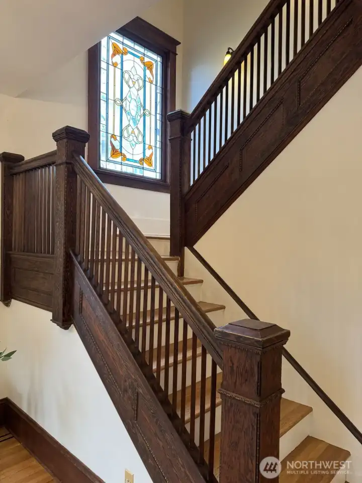 Original scrolled railings and stained glass window lead to upstairs