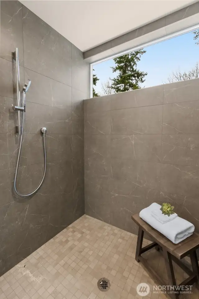 A bathroom that balances modern style with natural touches. Notice the oversized glass shower with sleek tiling and the large window flooding the space with light—a serene retreat to start and end your day.