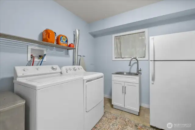 Large laundry room on the lower floor with utility sink and fridge.