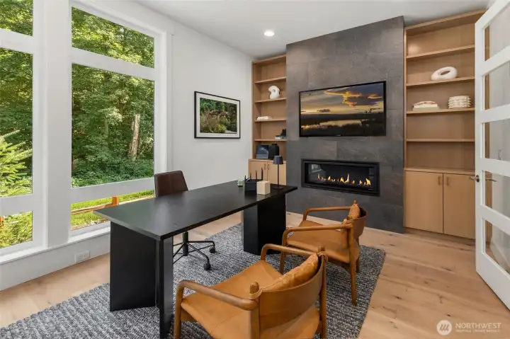 Formal office off of the entry hallway features, glass paneled french doors, wide plank hardwood floors, floor to ceiling tile surround contemporary fireplace, and custom built in cabinets and shelving