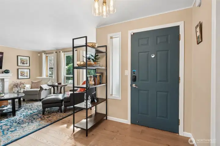 First impressions matter and this one shows up looking pulled together. The engineered hardwood floors set the tone right away, smooth, warm, and in that sweet spot of modern but timeless. White trim frames everything cleanly while the long privacy glass window by the front door lets light pour in like it owns the place, minus the neighborhood audience. The crackle glass light fixture overhead adds just enough personality to feel intentional, like someone actually thought about lighting beyond the big box aisle. Sightlines carry straight into the living room where triple windows overlook the front yard and flood the space with daylight, amplified by bright white ceilings and creamy latte walls that soften the whole vibe. It feels welcoming, elevated, and easy to picture yourself walking in every single day.