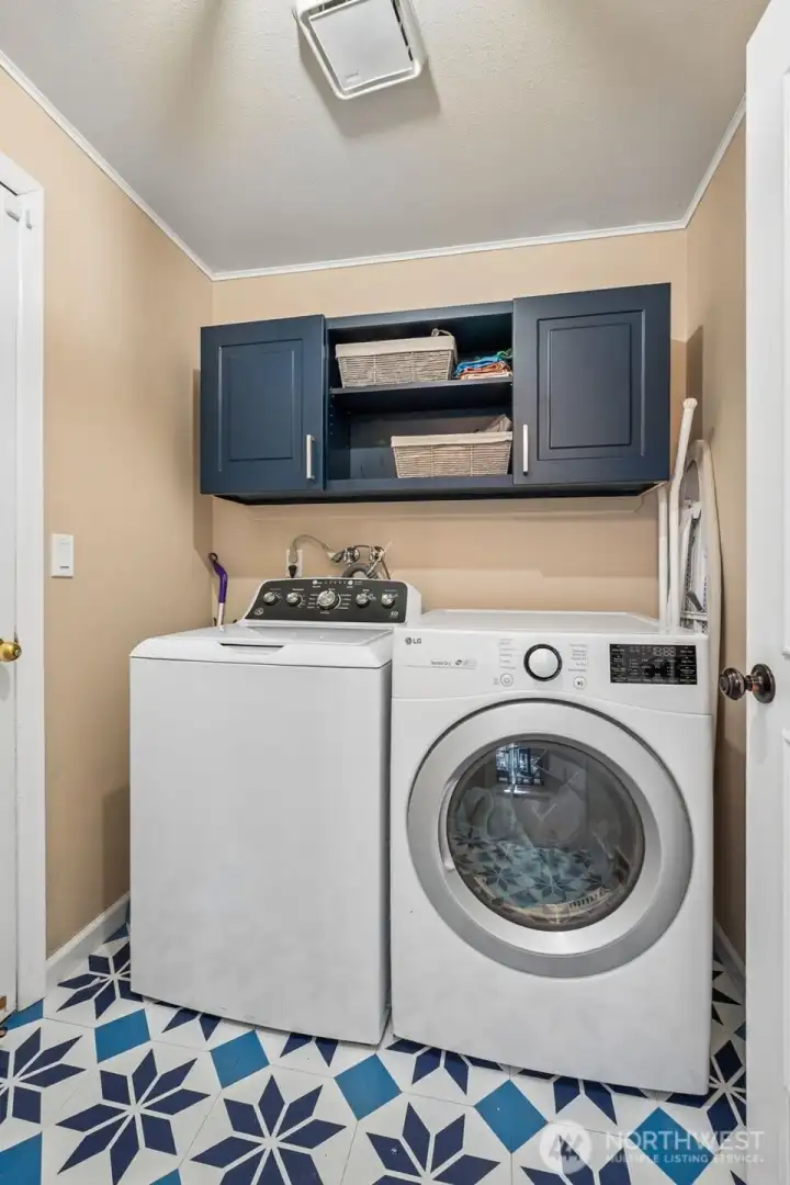 Who said laundry rooms have to be boring. This one is serving mood and practicality in equal measure with striking teal storage cabinetry that feels bold in the best way. Soft latte walls keep the palette grounded, and the patterned blue and white flooring brings just enough visual energy to make the whole space feel intentional. With direct access to the garage through the door on the left, this becomes a natural transition zone for coats, bags, and everyday chaos. Plenty of cabinetry helps keep things organized, so the routine stuff of life happens in a space that actually feels enjoyable. Washer and dryer included!