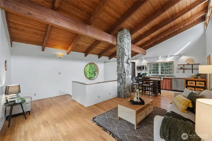 Upstairs, the main living space is a true architectural highlight. Soaring vaulted ceilings clad in warm tongue-and-groove wood with exposed beams bring depth and character, while a striking stone column adds a sculptural focal point.