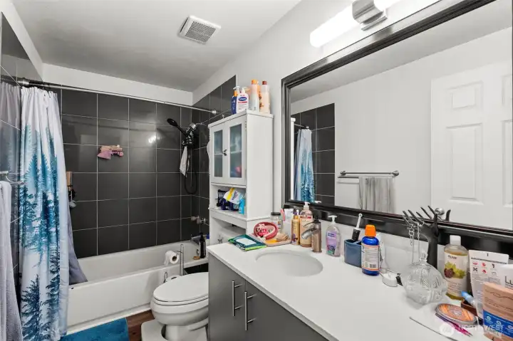 Clean, functional bathroom features a full tub and shower with tile surround and modern cabinetry.