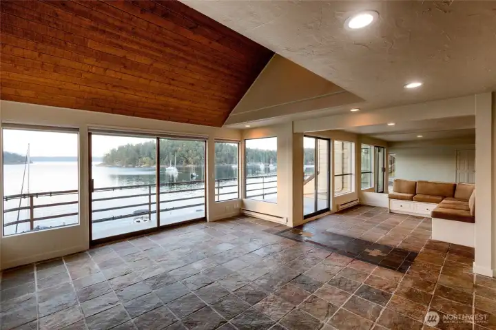 Dramatic waterfront great room is the heart of the home, where soaring vaulted tongue-and-groove cedar ceilings, rich natural slate floors, and an expansive wall of glass frame tranquil marina and harbor views. A wide sliding glass door opens to the spacious waterfront deck, creating seamless indoor-outdoor living. The open design flows effortlessly into the chef's kitchen and built-in banquette, making this an exceptional space for entertaining or simply enjoying the peaceful rhythm of island life. Dramatic waterfront great room is the heart of the home, where soaring vaulted tongue-and-groove cedar ceilings, rich natural slate floors, and an expansive wall of glass frame tranquil marina and harbor views. A wide sliding glass door opens to the spacious waterfront deck, creating seamless indoor-outdoor living. The open design flows effortlessly into the chef's kitchen and built-in banquette, making this an exceptional space for entertaining or simply enjoying the peaceful rhythm of island life.