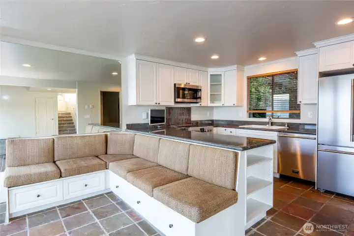 Renovated chef's kitchen is designed for both everyday living and entertaining, featuring premium Fulgor Milano appliances, dramatic natural granite countertops, custom ceiling-height cabinetry, and an expansive peninsula overlooking the waterfront great room. A custom-built banquette with integrated storage creates an inviting dining space where family and friends naturally gather. Rich natural slate flooring adds timeless Northwest character and complements virtually any design style Renovated chef's kitchen is designed for both everyday living and entertaining, featuring premium Fulgor Milano appliances, dramatic natural granite countertops, custom ceiling-height cabinetry, and an expansive peninsula overlooking the waterfront great room. A custom-built banquette with integrated storage creates an inviting dining space where family and friends naturally gather. Rich natural slate flooring adds timeless Northwest character and complements virtually any design style