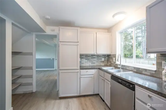 The kitchen is bathed in natural light pouring through the expansive window. Ample cabinets cater to all your kitchen essentials, complemented by additional shelving for added convenience. Through the doorway lies the recreational room.