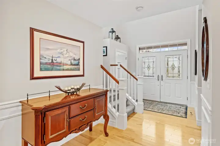 The entry showcases Birch hardwood floors and crisp millwork, creating an immediate sense of refinement as you step inside. The fiberglass double doors with decorative glass panels fill the space with natural light and set an elegant tone for the home.