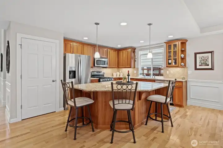 The kitchen features Shaker cherry cabinets crowned with elegant molding, granite counters, and a spacious island that anchors the room beautifully. Stainless steel appliances—including the Whirlpool refrigerator, Bosch dishwasher, and Maytag gas stove—add a polished, modern touch while the pantry to the left provides excellent household storage.